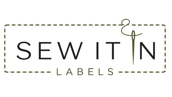 The logo for Sew It Labels, featuring the words 'SEW IT' in black serif letters and 'LABELS' in a smaller olive green serif font, enclosed in a dashed rectangular border with a stylized sewing needle and ampersand graphic.